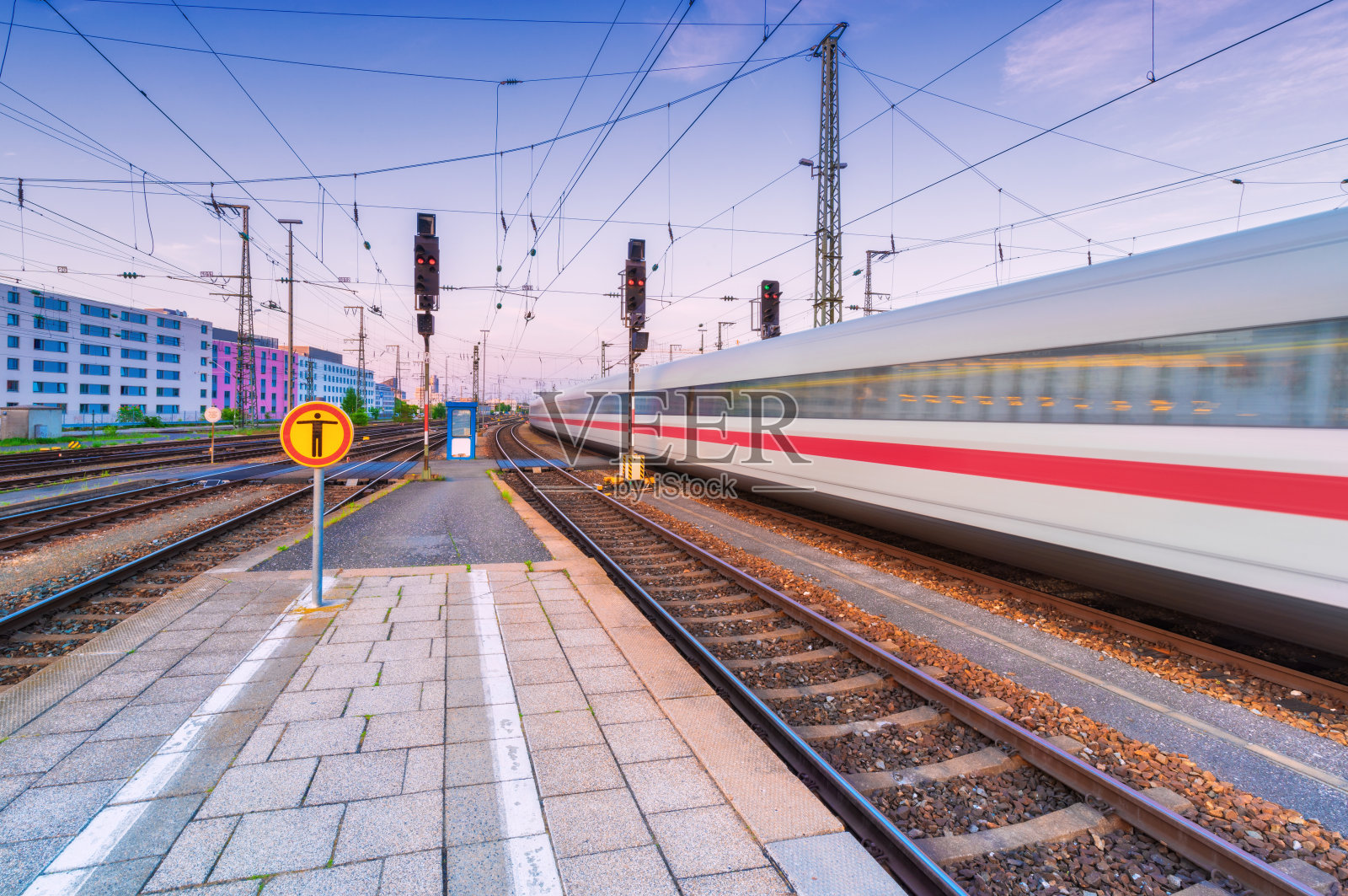 日落时分，高速列车在火车站上行驶。在欧洲的铁路站台上移动的模糊的现代城际列车。客运铁路运输。铁路在《暮光之城》。旅行照片摄影图片