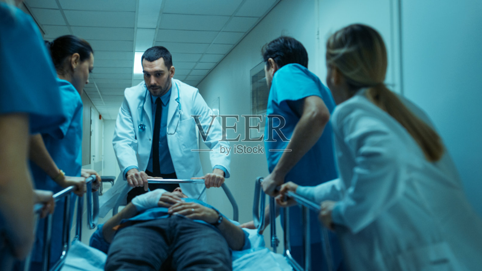 急诊科医生，护士和外科医生通过医院走廊移动躺在轮床上的严重受伤的病人。医护人员匆忙将病人转移到手术室。照片摄影图片