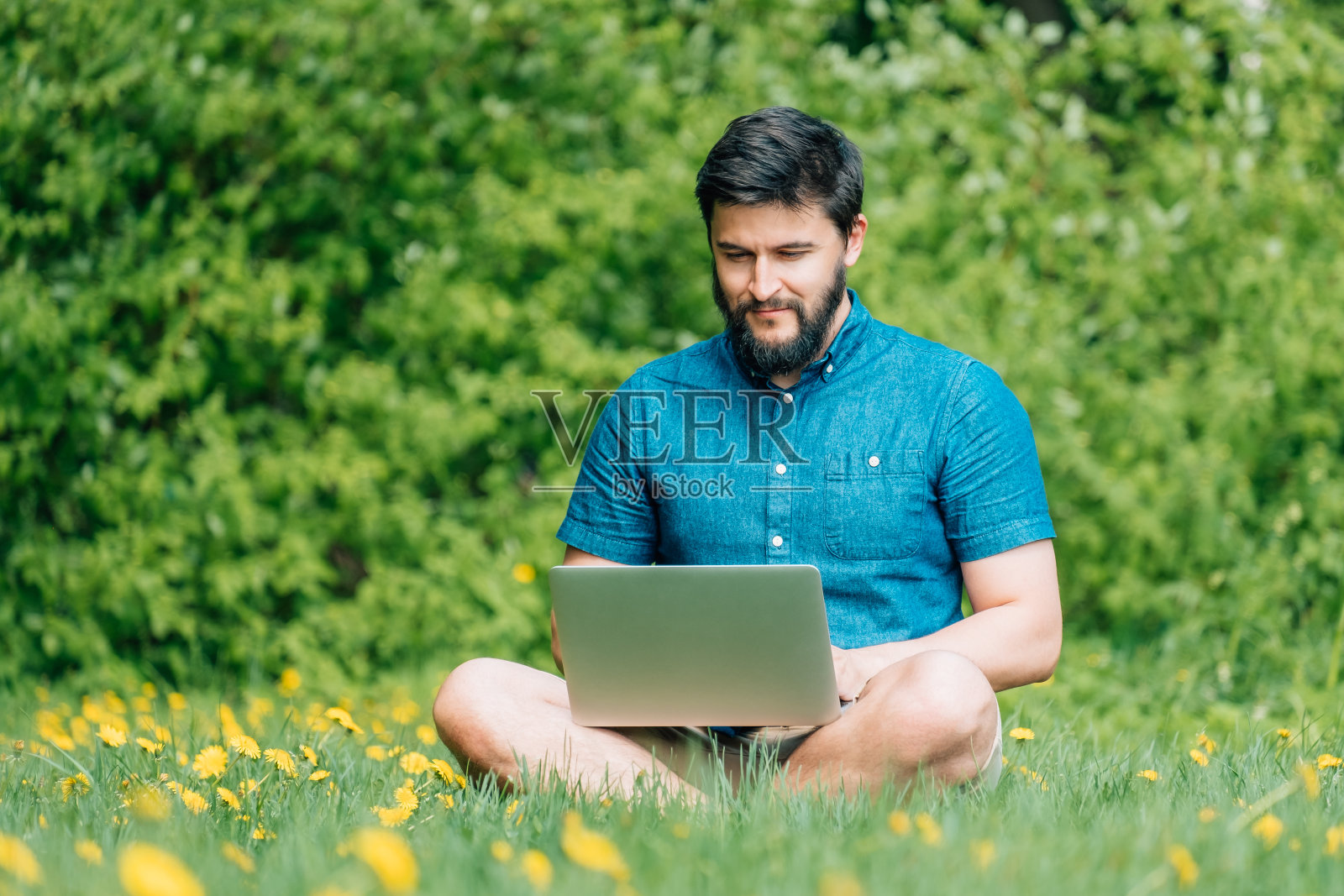 一个快乐的嬉皮士，带着笔记本电脑坐在户外的绿草地上。自由的概念照片摄影图片