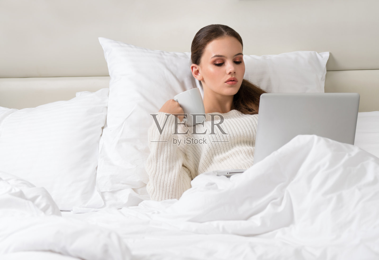 美丽迷人的年轻白人女人黑发早上在白色的床上与杯子在手提电脑脸照片摄影图片