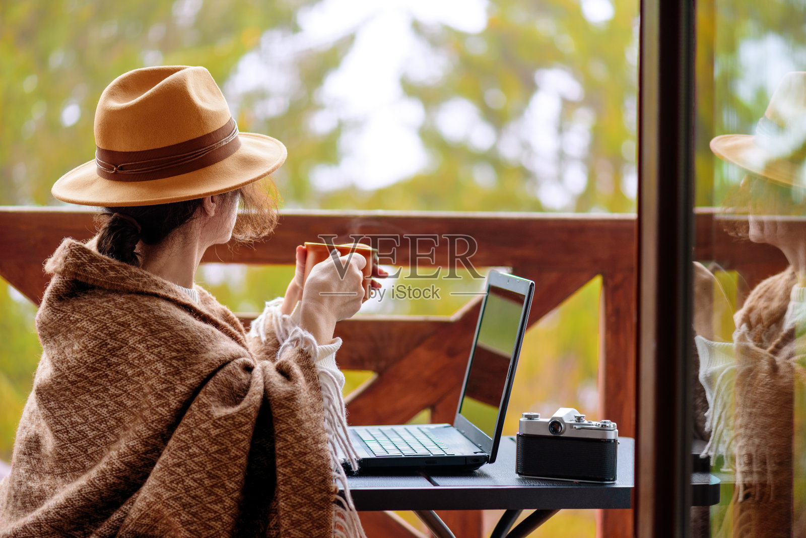 年轻的自由职业女性坐在露台上，拿着笔记本电脑喝着茶。照片摄影图片