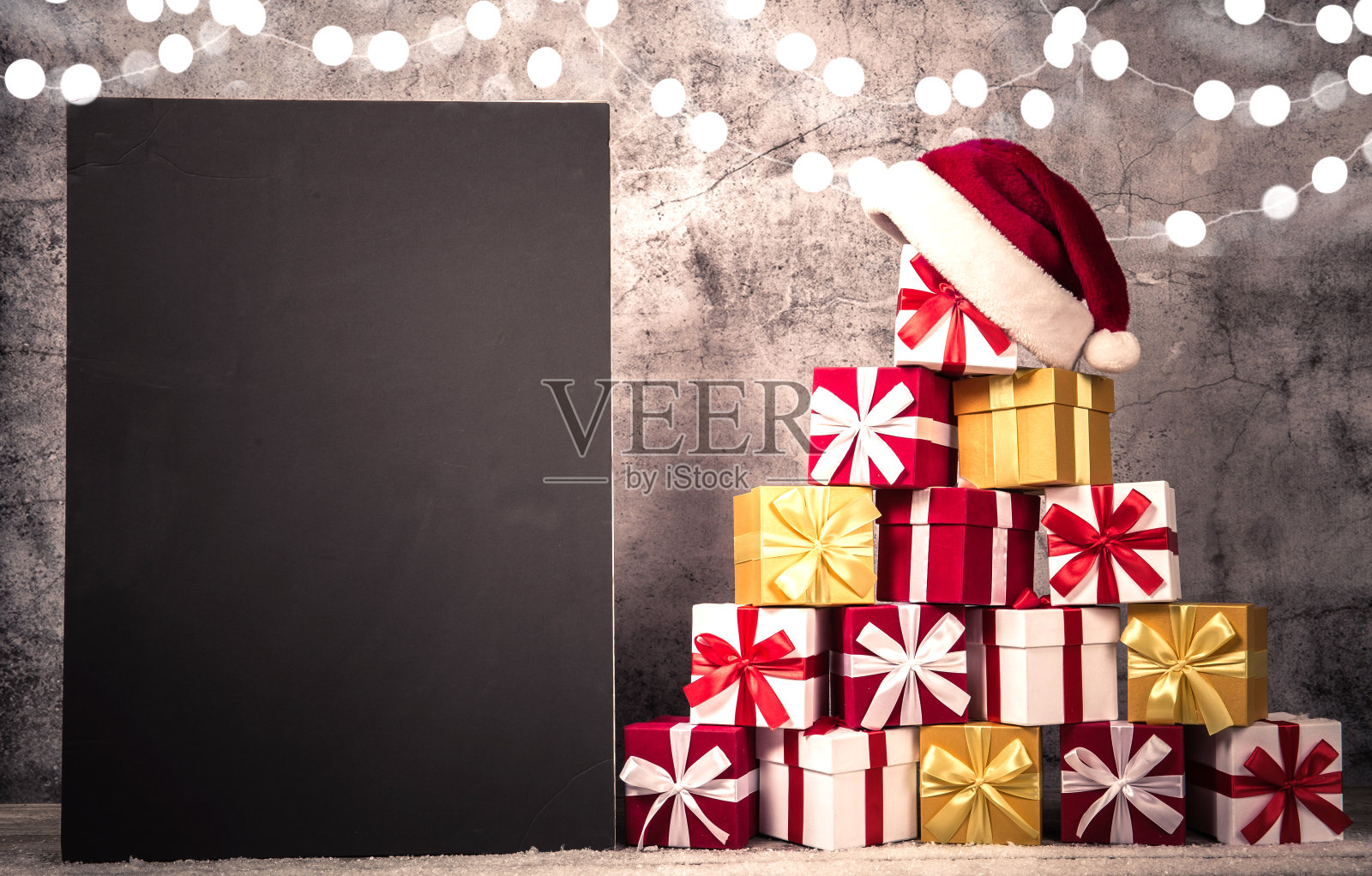 圣诞礼盒在金字塔形状的混凝土墙前面，上面有圣诞老人的帽子。查看与复制空间为您的文本照片摄影图片