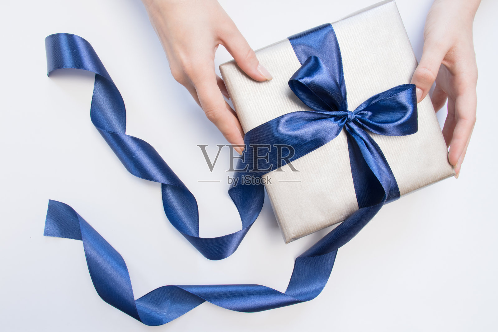 礼盒与蓝色蝴蝶结在一个女人的手在孤立的背景。假期的概念。照片摄影图片