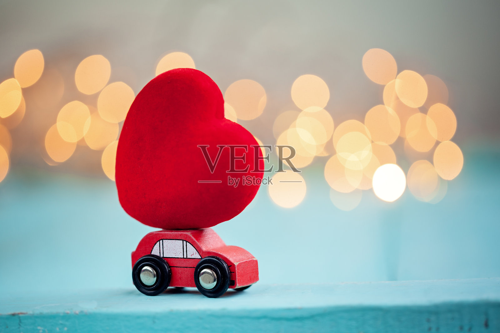 微缩红色小车载着一颗红色的大心在闪亮的散焦背景上。照片摄影图片