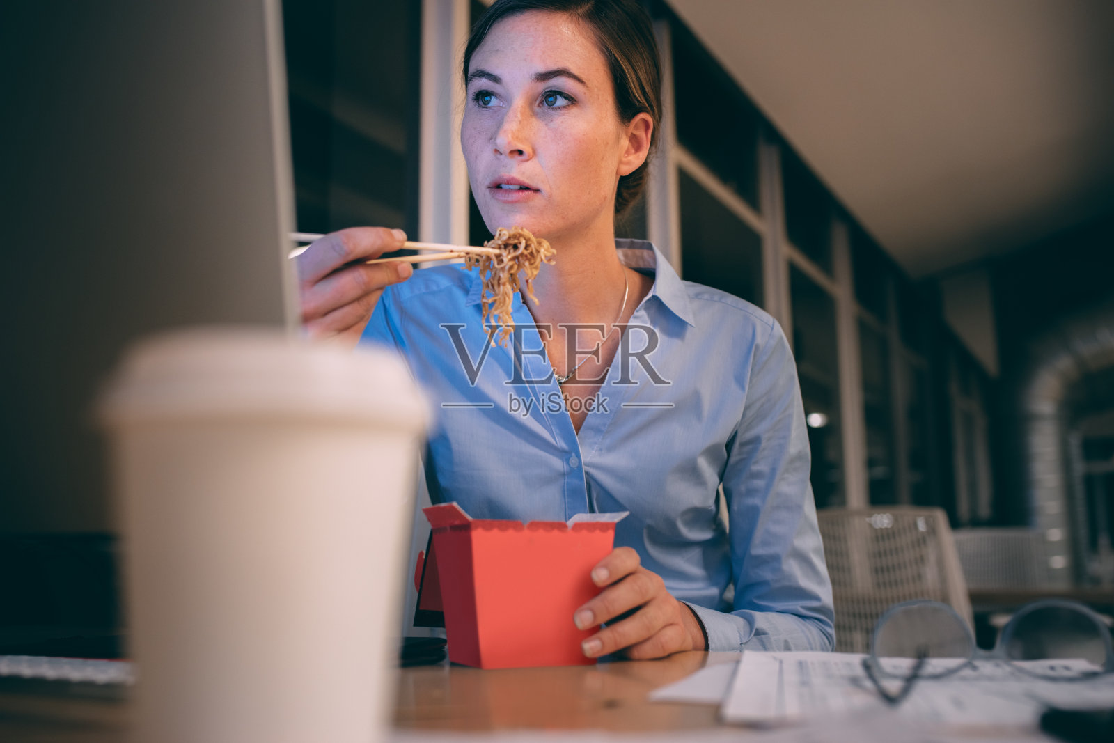 女商人一边吃饭一边在办公室工作到很晚照片摄影图片