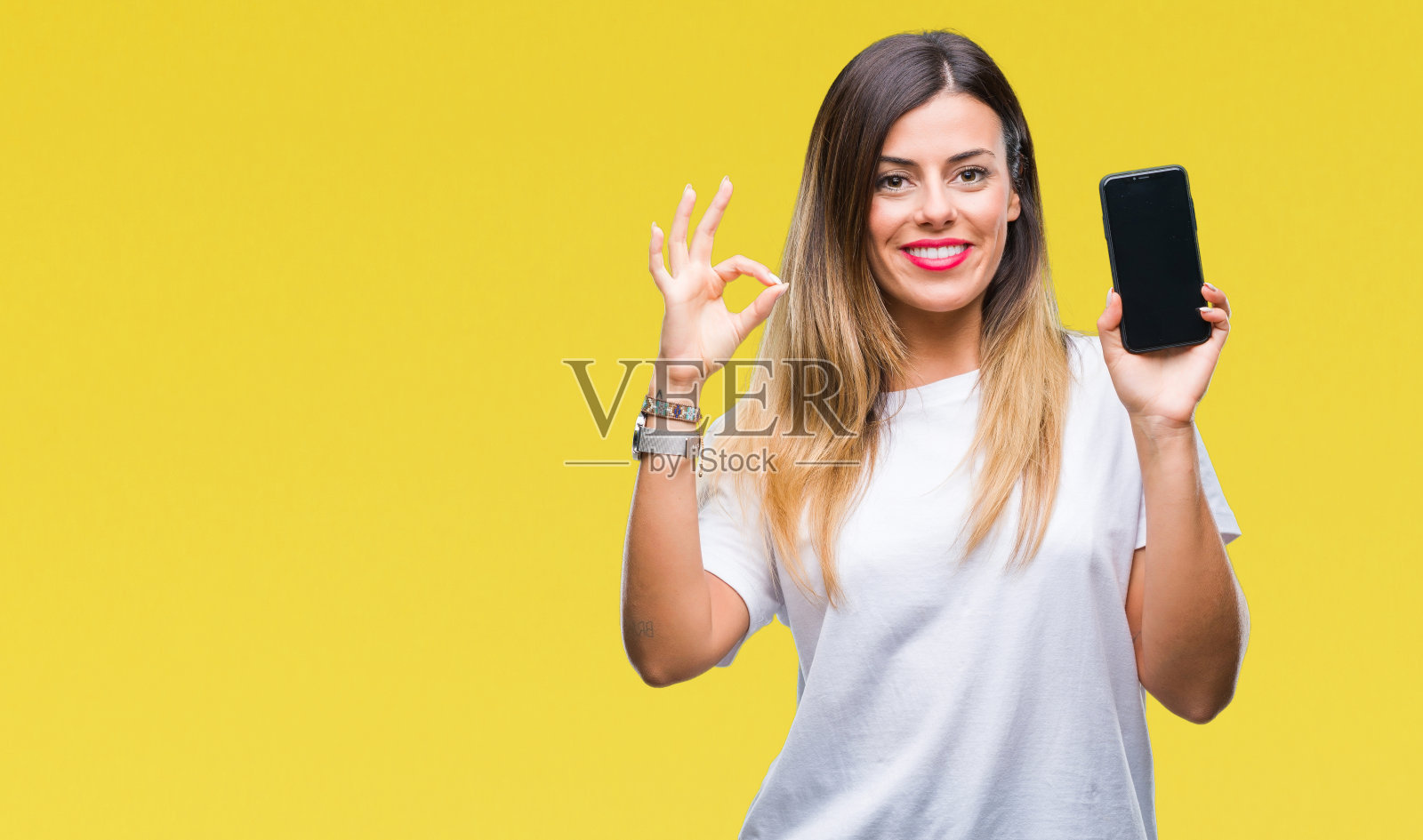 年轻漂亮的女人在孤立的背景下展示智能手机的空白屏幕，用手指做ok手势，很好的符号照片摄影图片