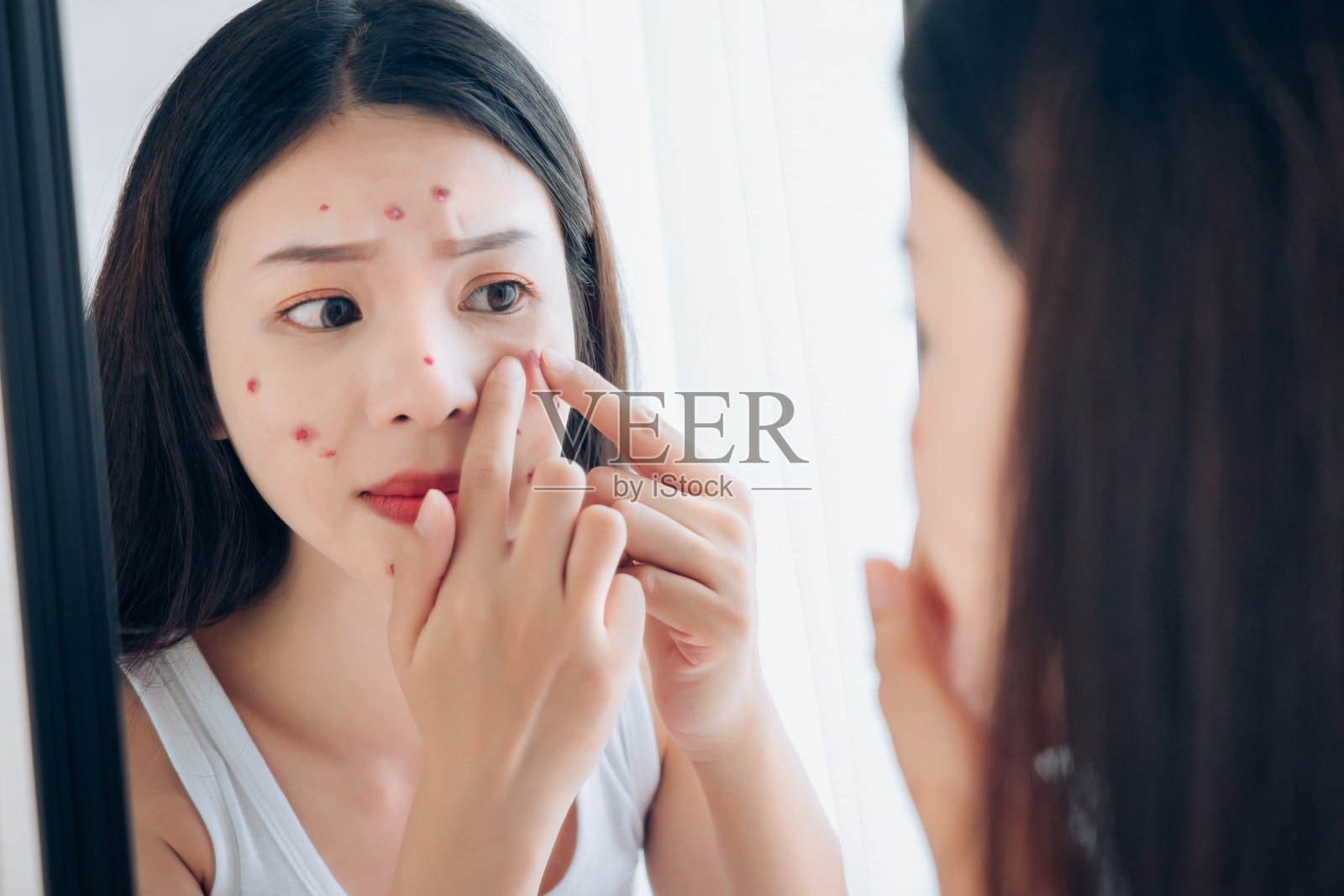 年轻的亚洲女人在照镜子时脸上挤痘痘问题她没有护肤。照片摄影图片
