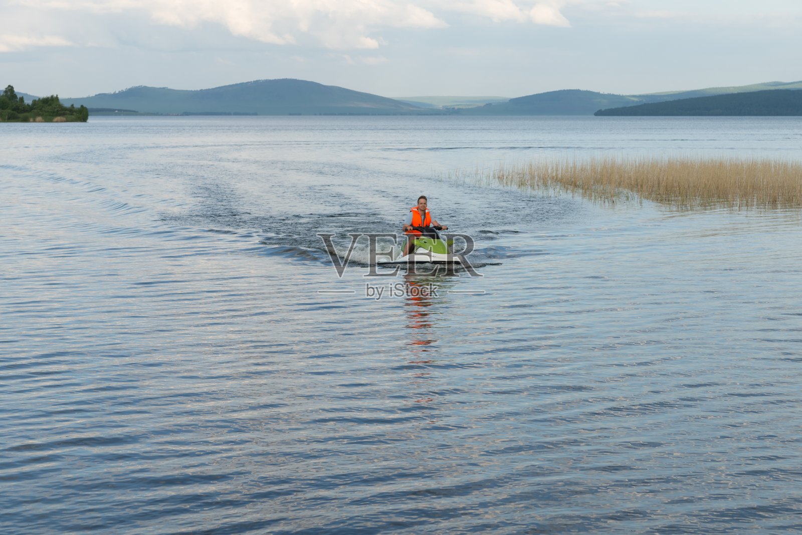 夏天，一个穿着救生衣的年轻人在湖上骑水上自行车。照片摄影图片