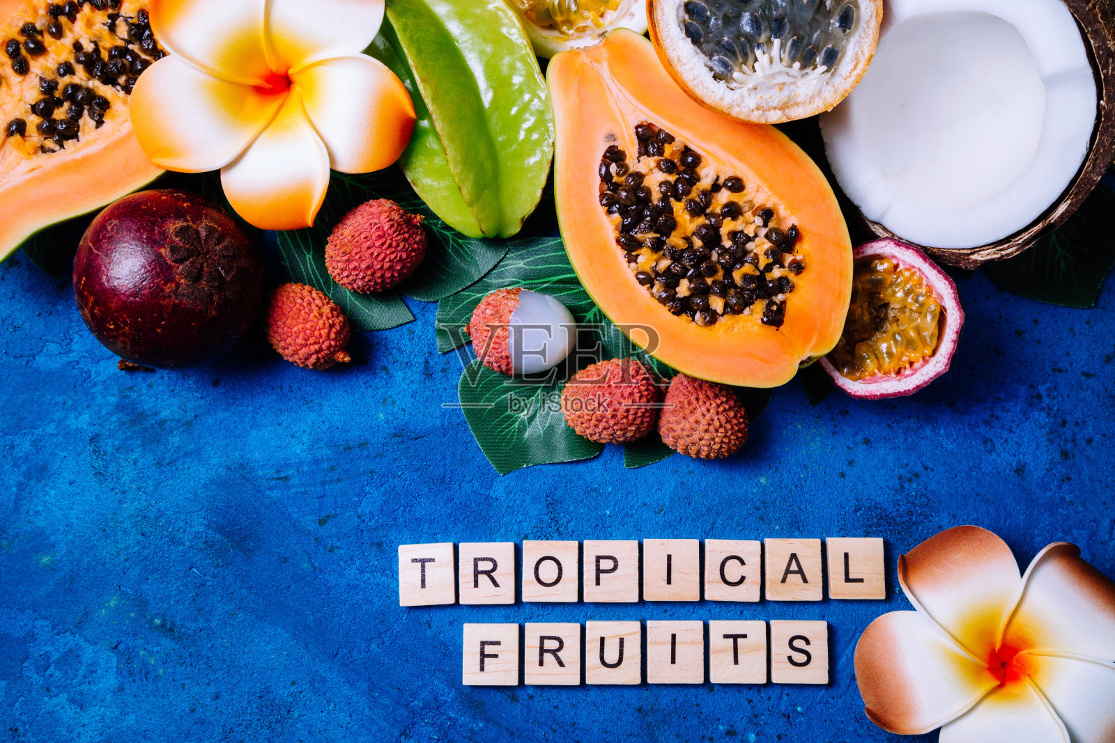 夏日的热带背景，奇异的各种水果，绿色的棕榈叶和蓝色的花朵。水果的背景照片摄影图片