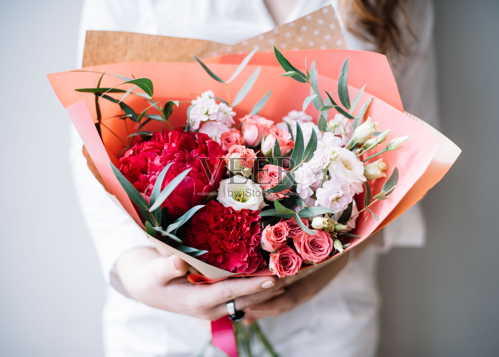 非常漂亮的年轻女子手持一束美丽的鲜花盛开的新鲜牡丹，玫瑰，丁香，马提奥拉，康乃馨，桉树在鲜艳的粉红色和白色的颜色在灰色的墙壁背景照片摄影图片
