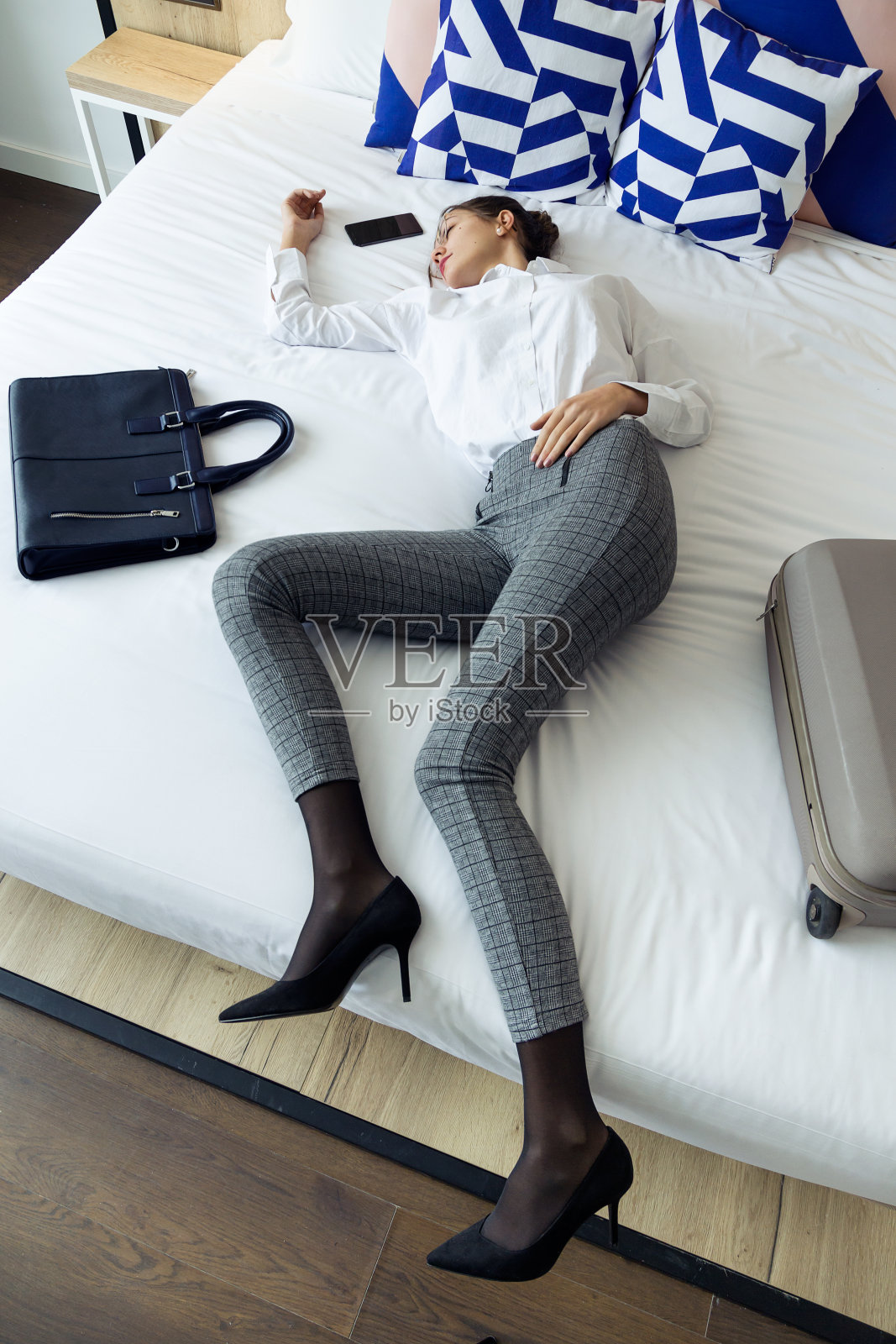 疲惫的年轻女商人穿着西装在酒店房间的床上休息一天的辛苦工作。照片摄影图片