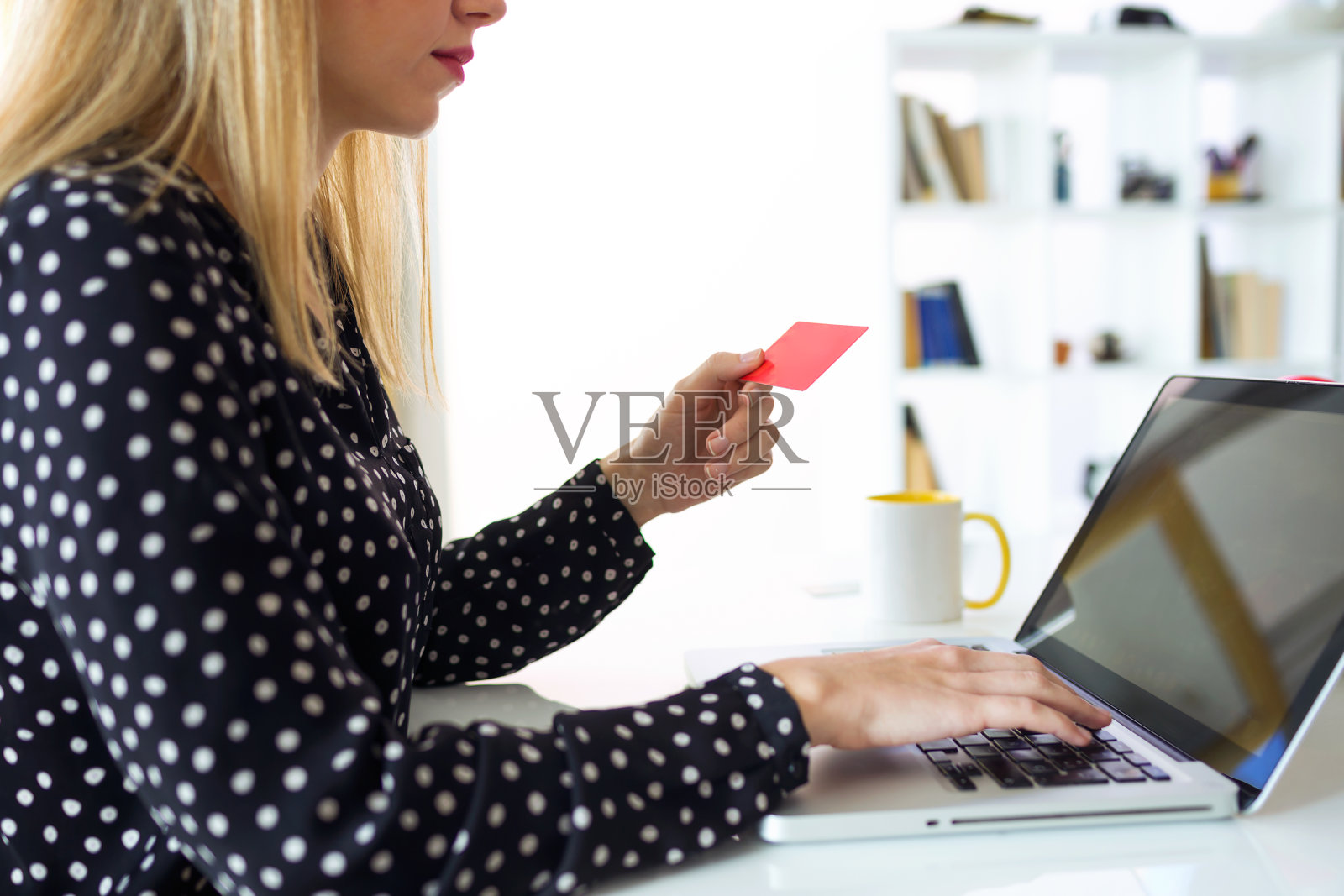自信的年轻女子拿着红色的信用卡，在家里用电脑在网上购物。照片摄影图片