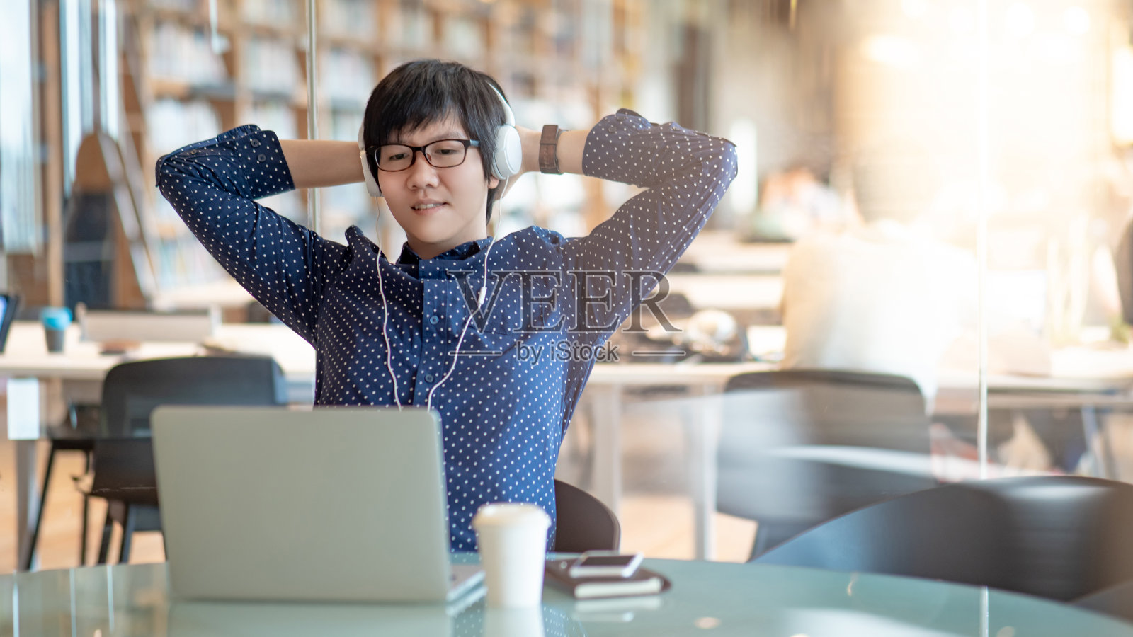 一位戴眼镜的亚洲年轻人喜欢在公共图书馆边听音乐边用笔记本电脑工作。在大学里做研究的男大学生。教育机会和自我学习照片摄影图片