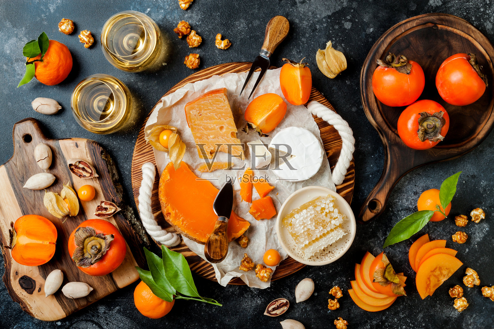 各种奶酪板或拼盘配上奶酪，柿子，蜂蜜和坚果。黑石的背景。俯视图，平放照片摄影图片