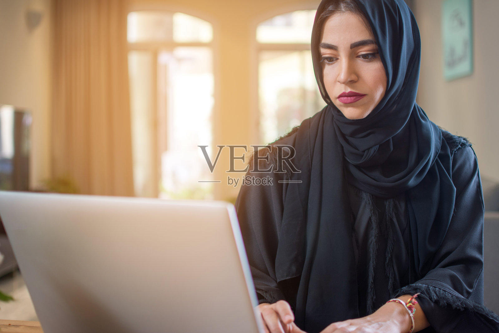 年轻的穆斯林妇女穿着阿拉伯长袍在家里使用笔记本电脑照片摄影图片
