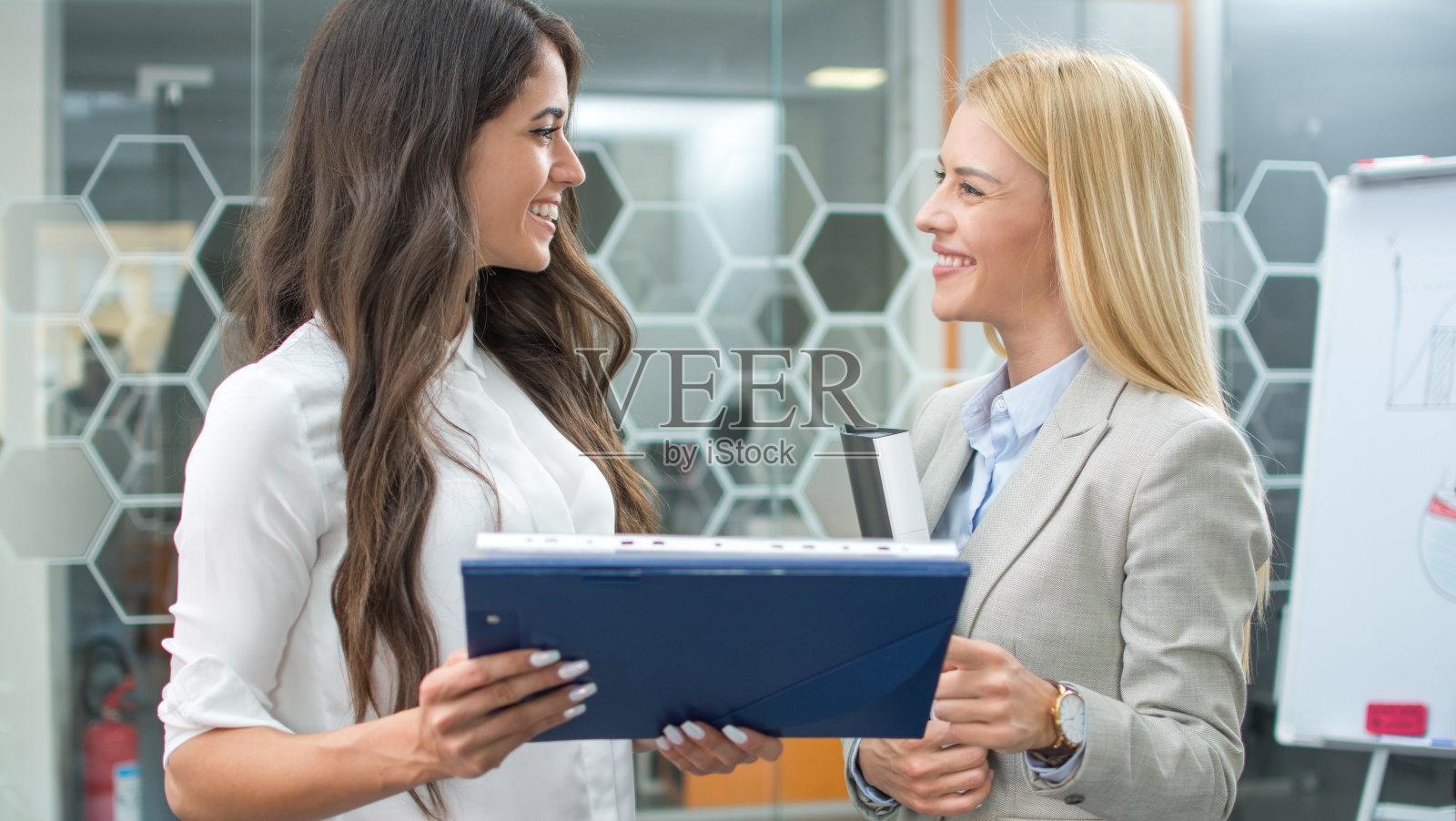 在一间现代化的办公室里，两个面带微笑的商务女性在开会讨论文件照片摄影图片