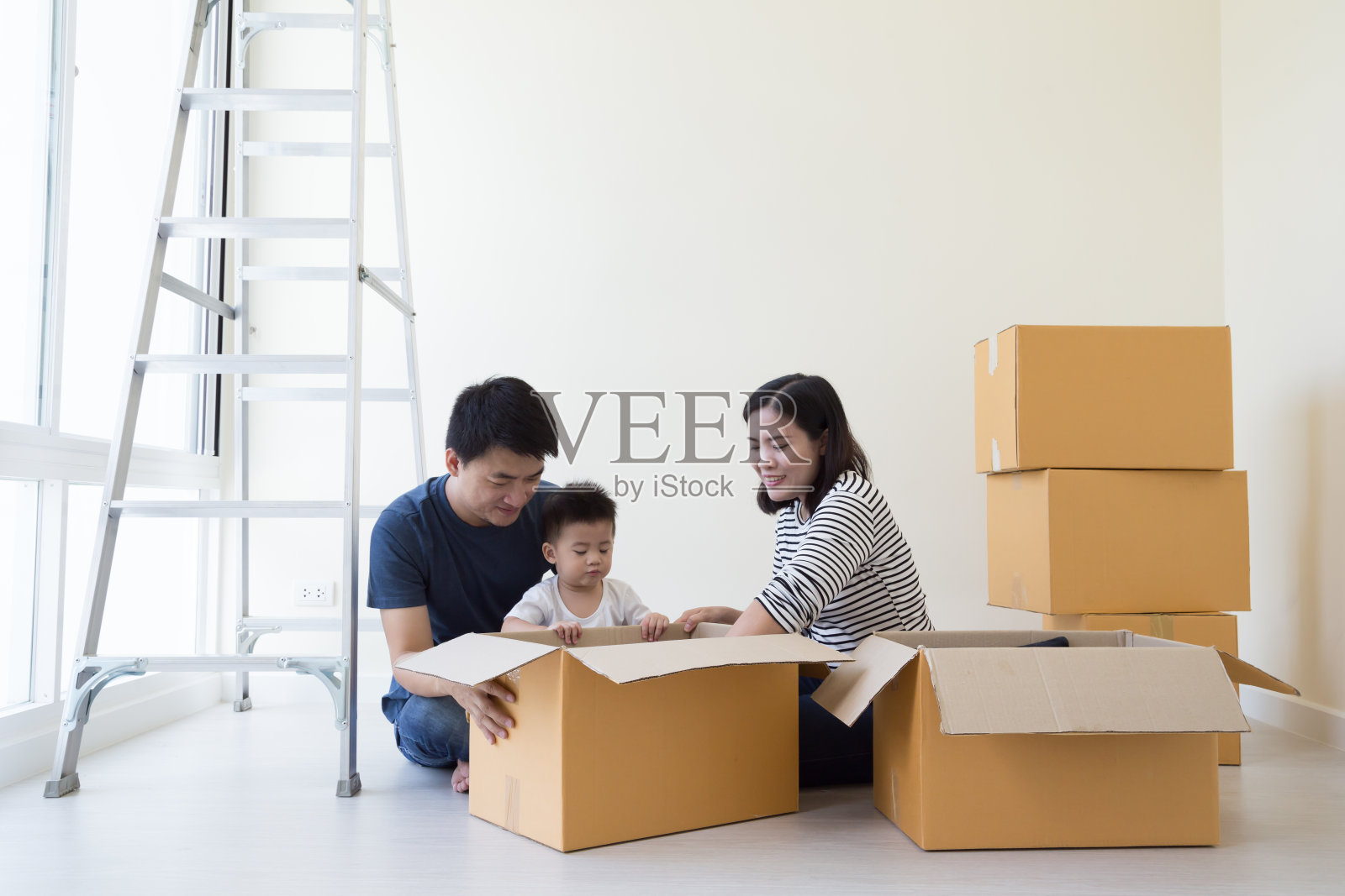 搬家那天，一家人在新家开箱，快乐的爸爸妈妈和儿子在新房子的卧室里玩着纸箱照片摄影图片