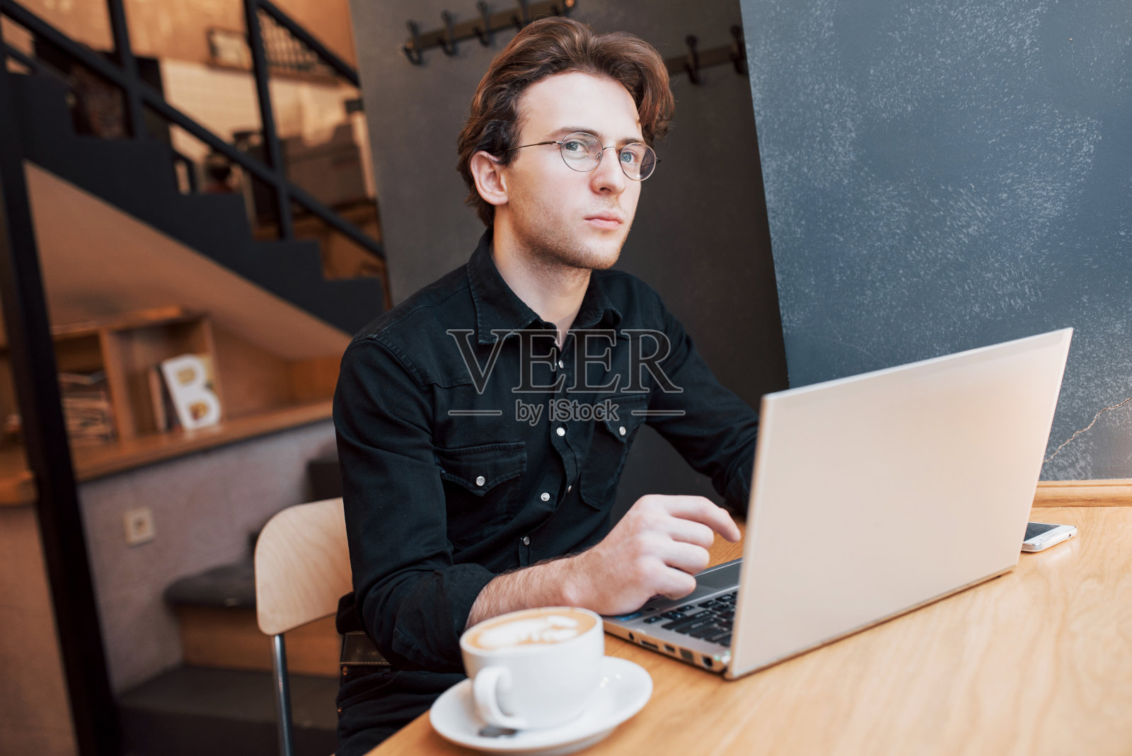 创造性的人设计师在他的笔记本电脑上工作，而等待在他最喜欢的咖啡馆室内，男学生在网上工作在现代咖啡馆室内早餐照片摄影图片