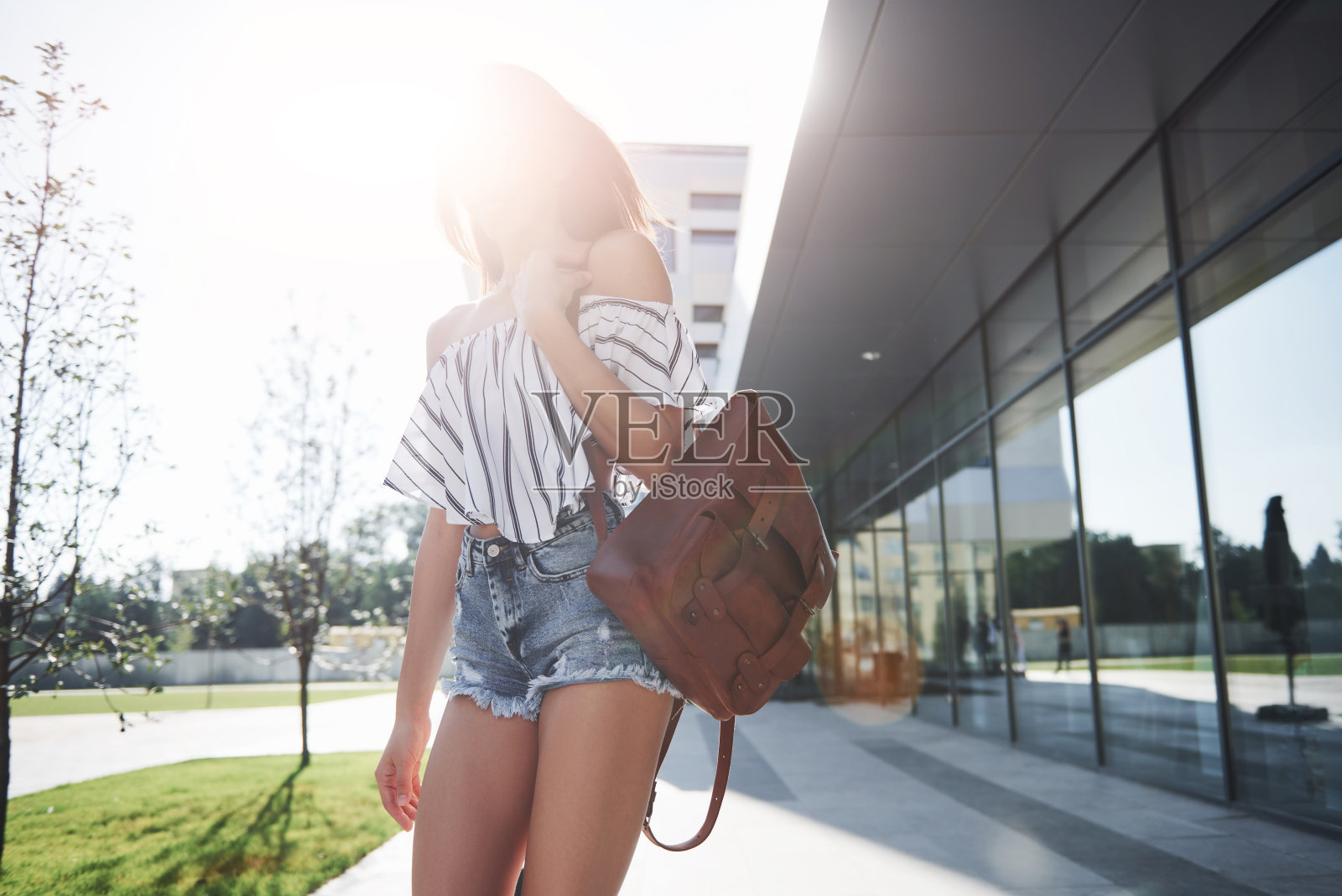 一个美丽的女孩背着背包，在一个阳光明媚的早晨走在城市的街道上照片摄影图片