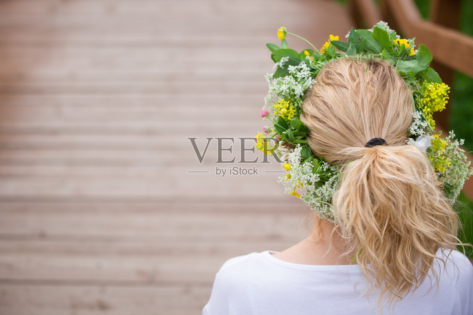 在一个温暖的夏日，美丽的金发碧眼的年轻女子戴着花圈在草地上。拿着野花花环的女孩在户外享受阳光。快乐的女人在花园里。生活方式,夏天的概念照片摄影图片