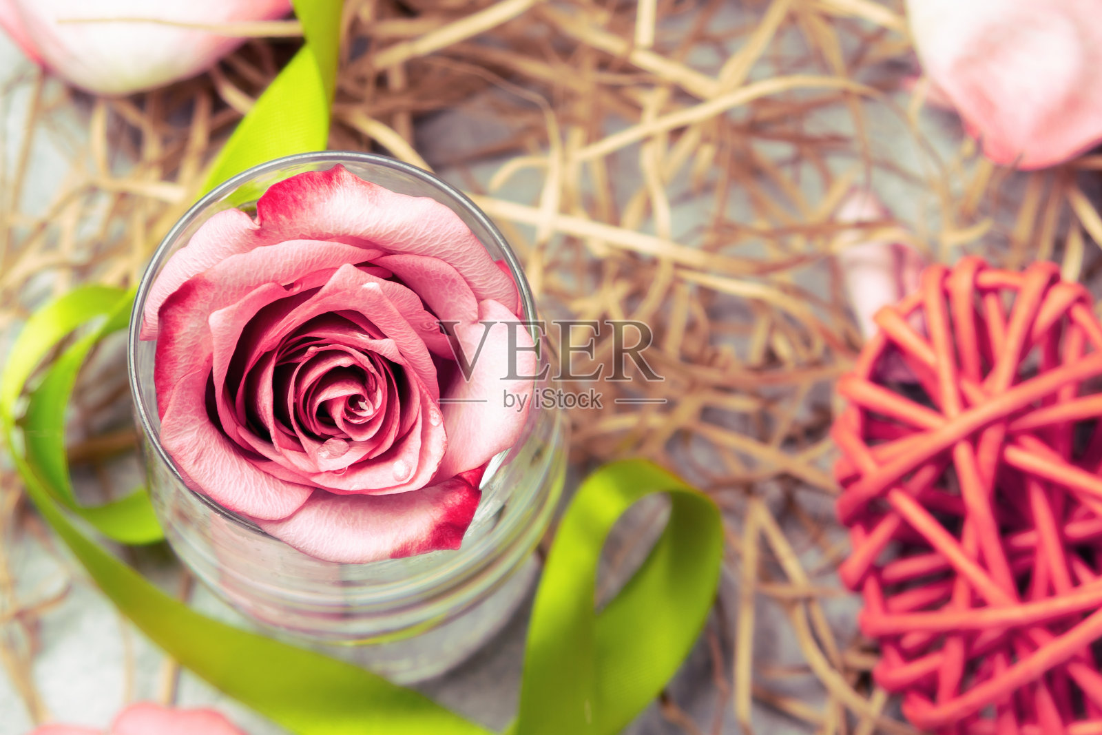 粉红玫瑰装在杯子里，桌上有水和装饰品照片摄影图片
