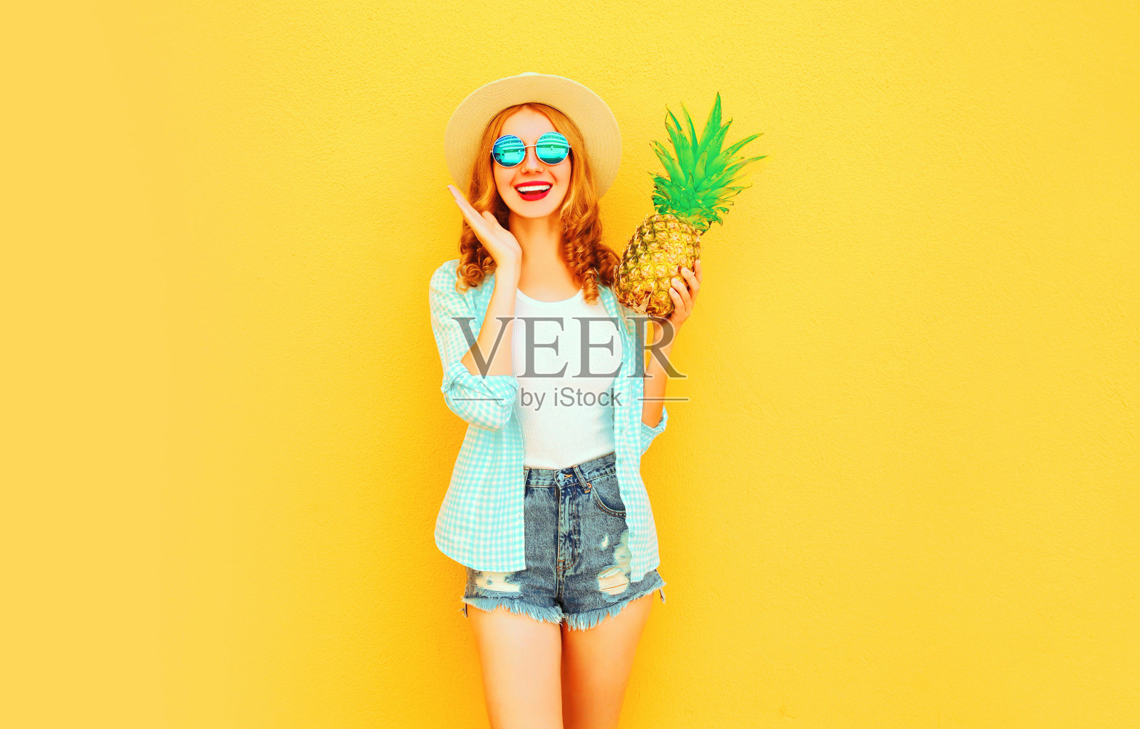 肖像快乐的微笑女人与菠萝有乐趣在夏天草帽，太阳镜，短裤上彩色的黄色背景照片摄影图片