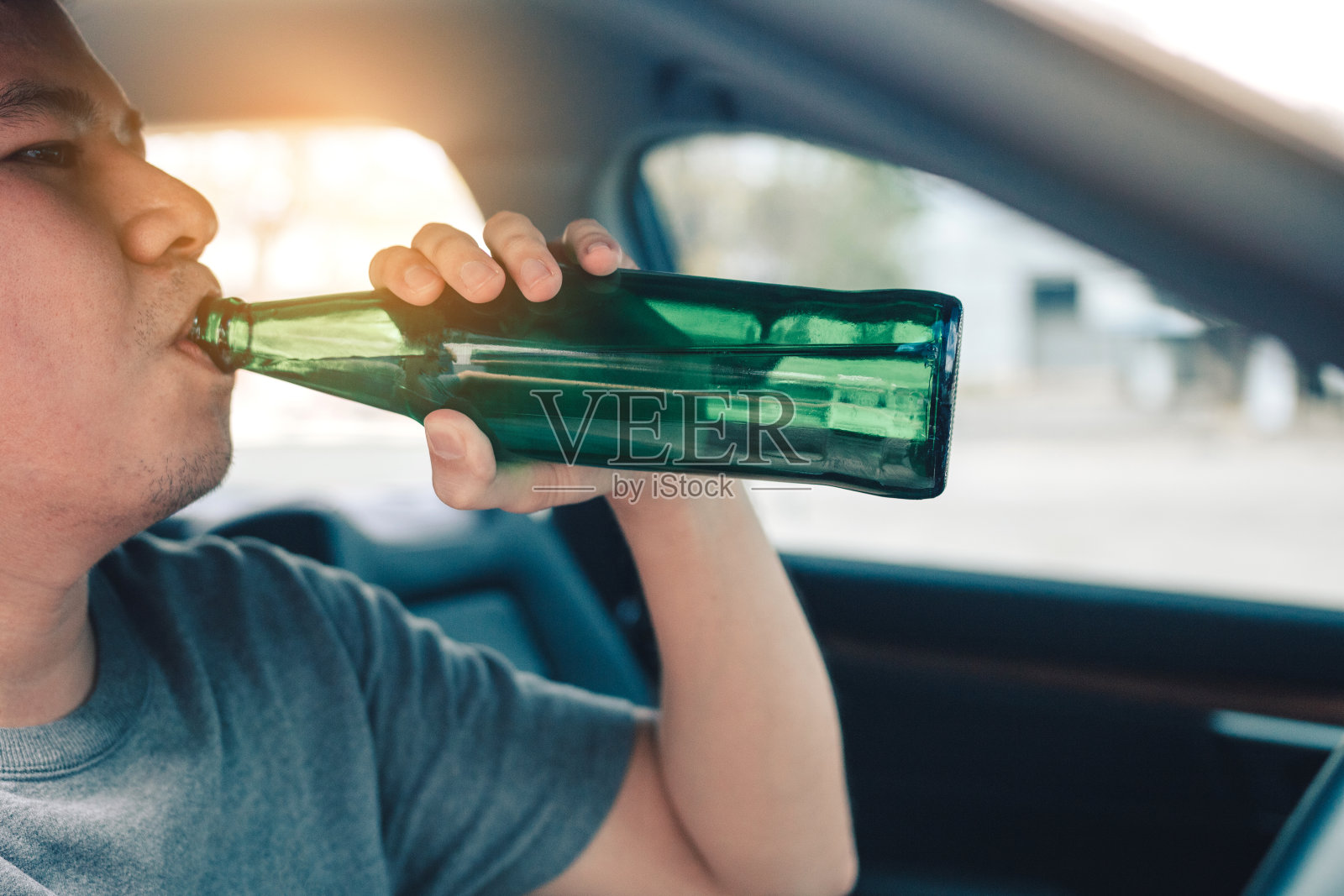 一个喝醉酒的亚洲人，一边开车一边喝啤酒。照片摄影图片