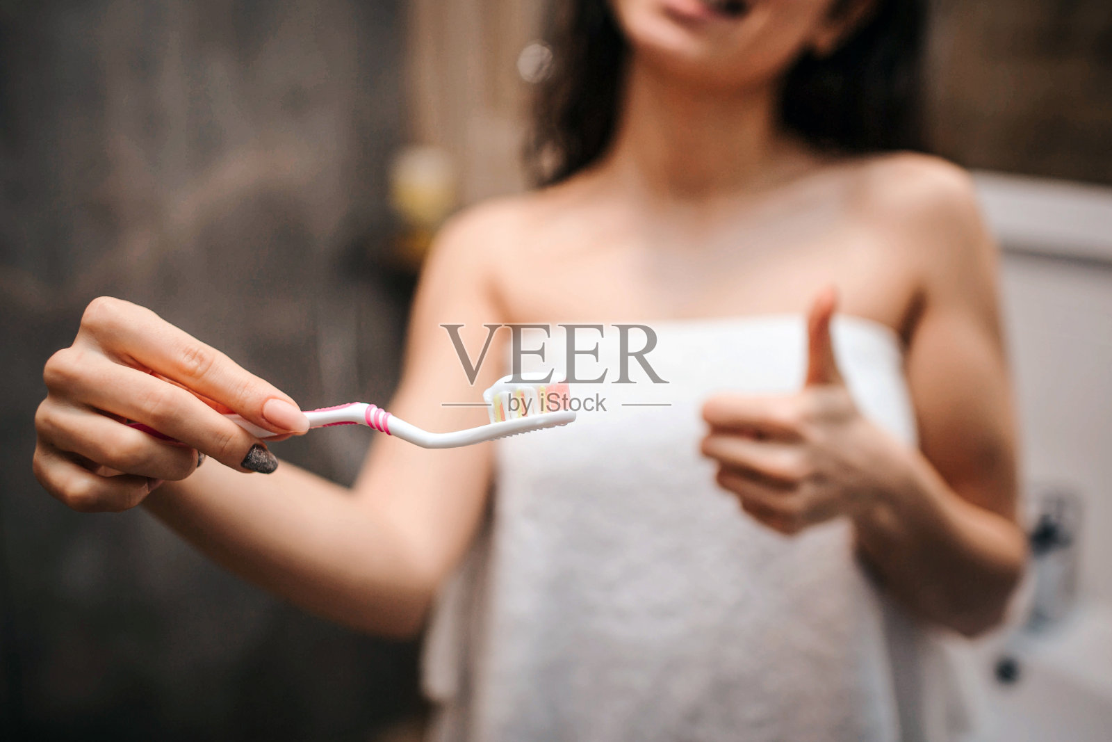 年轻的运动黑发美丽的女人做早上晚上例行对着镜子。剪视图模型在白色毛巾拿着牙刷与牙膏和大拇指向上。照片摄影图片