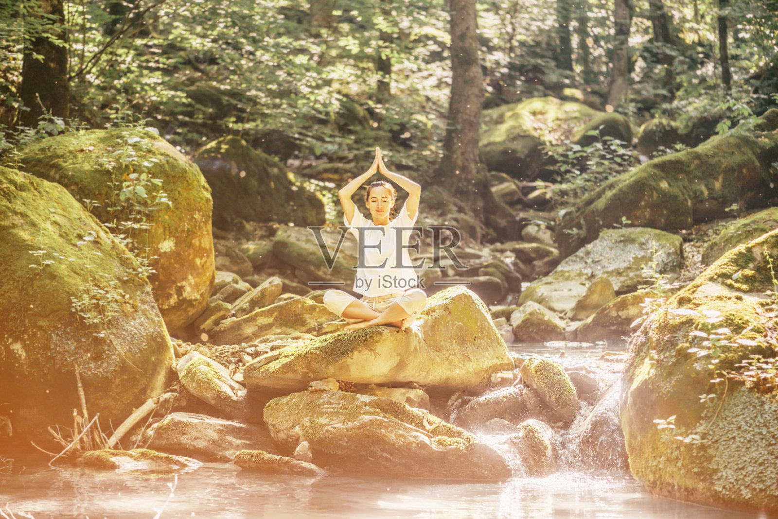 在河上的石头上莲花的姿势沉思的女人。照片摄影图片