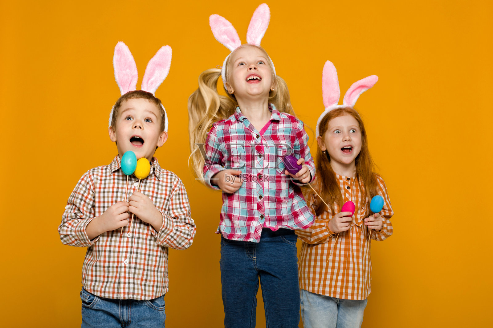 两个带着复活节兔子耳朵的小男孩和女孩，手里拿着五颜六色的彩蛋照片摄影图片