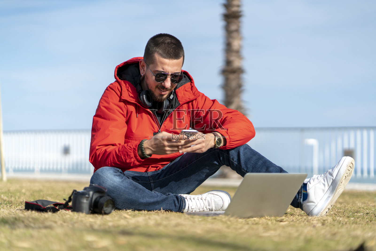 一个年轻人坐在草地上用笔记本电脑玩智能手机照片摄影图片