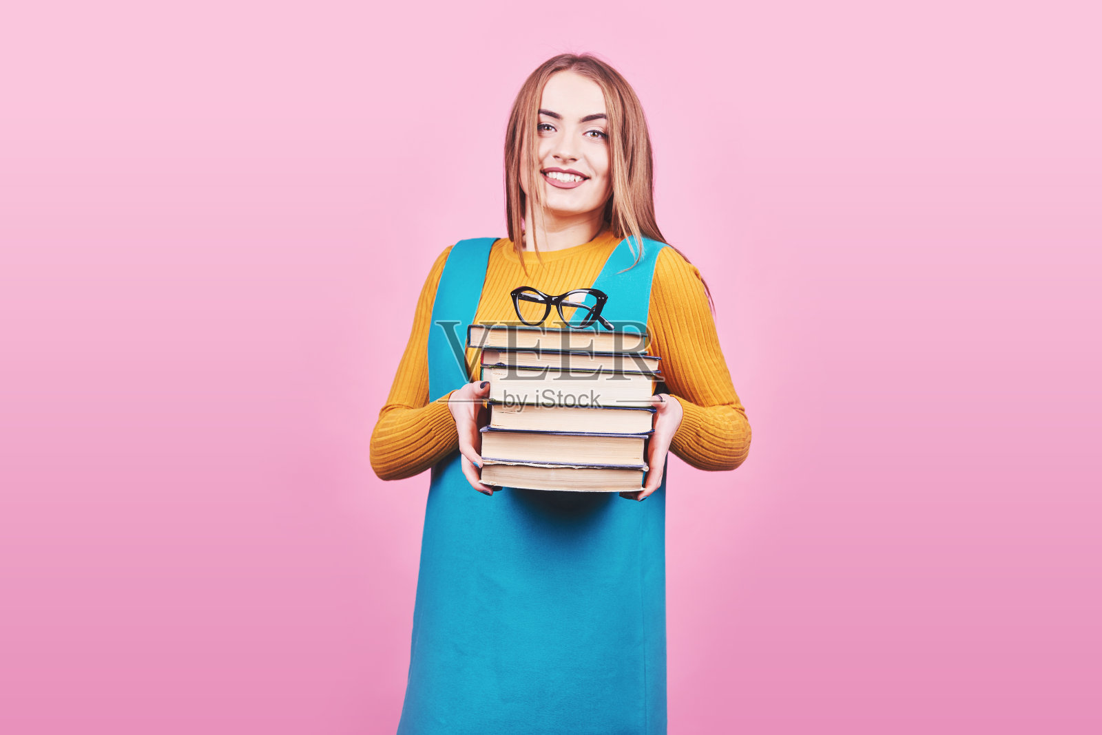快乐可爱的女孩手里拿着一堆书孤立在五颜六色的粉红色背景上。照片摄影图片
