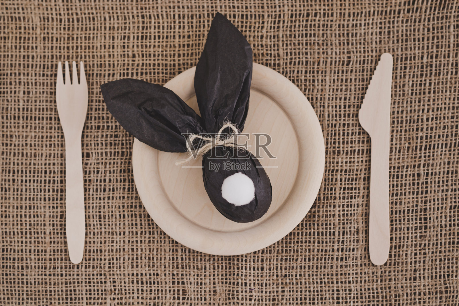 复活节兔子礼物鸡蛋包装在黑色的牛皮纸木制盘子，叉子和刀在麻袋布背景。照片摄影图片