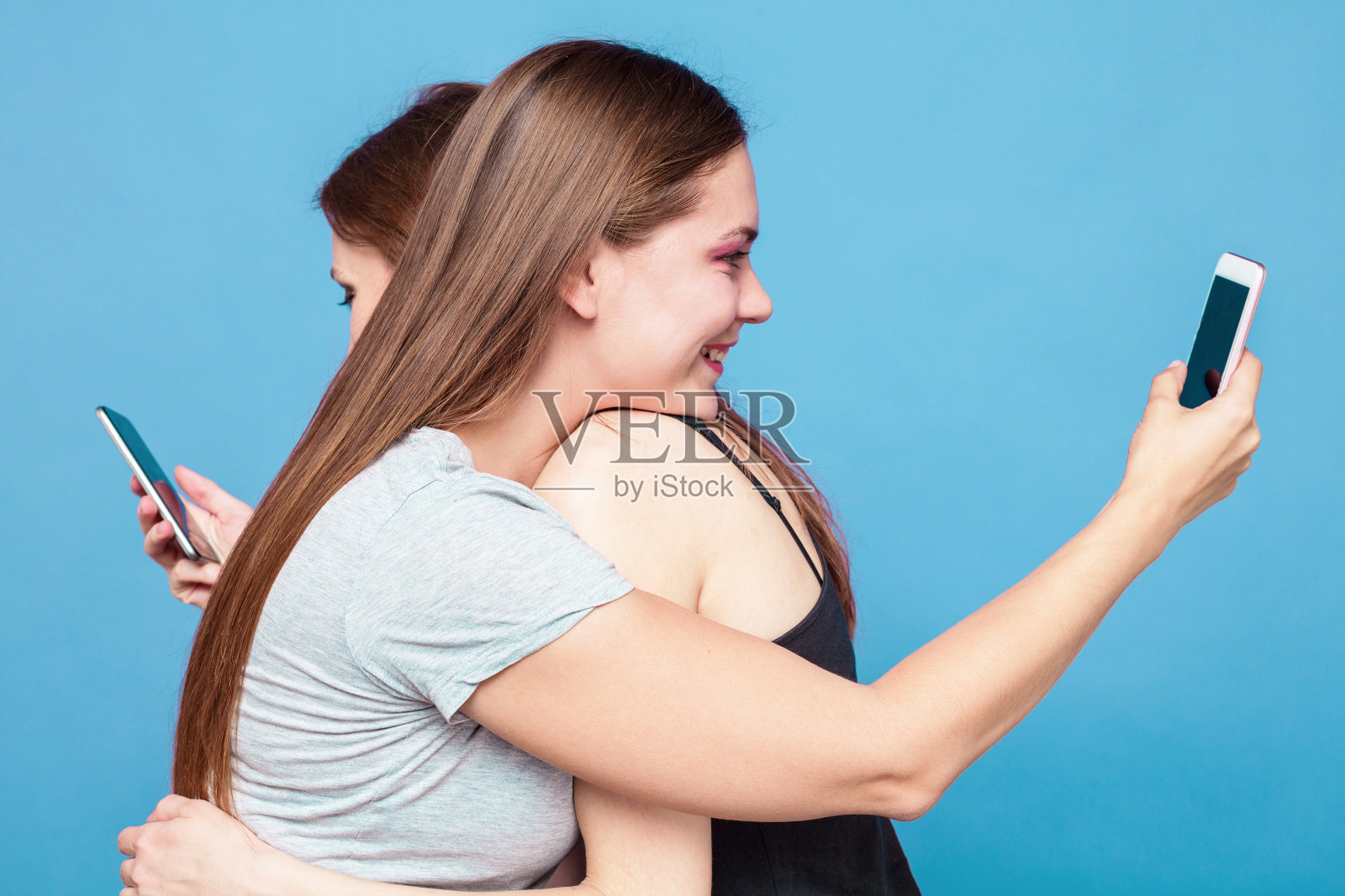 两个黑头发的年轻白种女人互相在背后用大胶带绑着什么东西。照片摄影图片