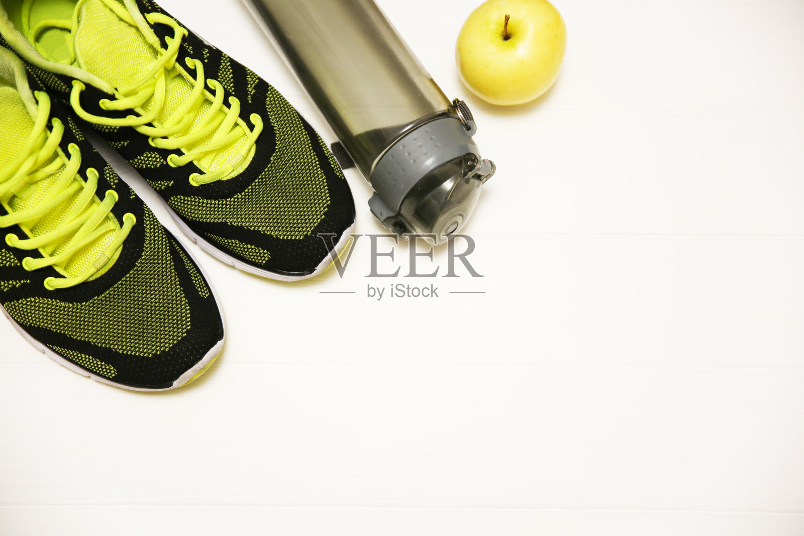 健康概念的照片。白色的木桌上放着运动鞋、一瓶水和水果苹果。健康的生活方式。运动动机的背景。照片摄影图片