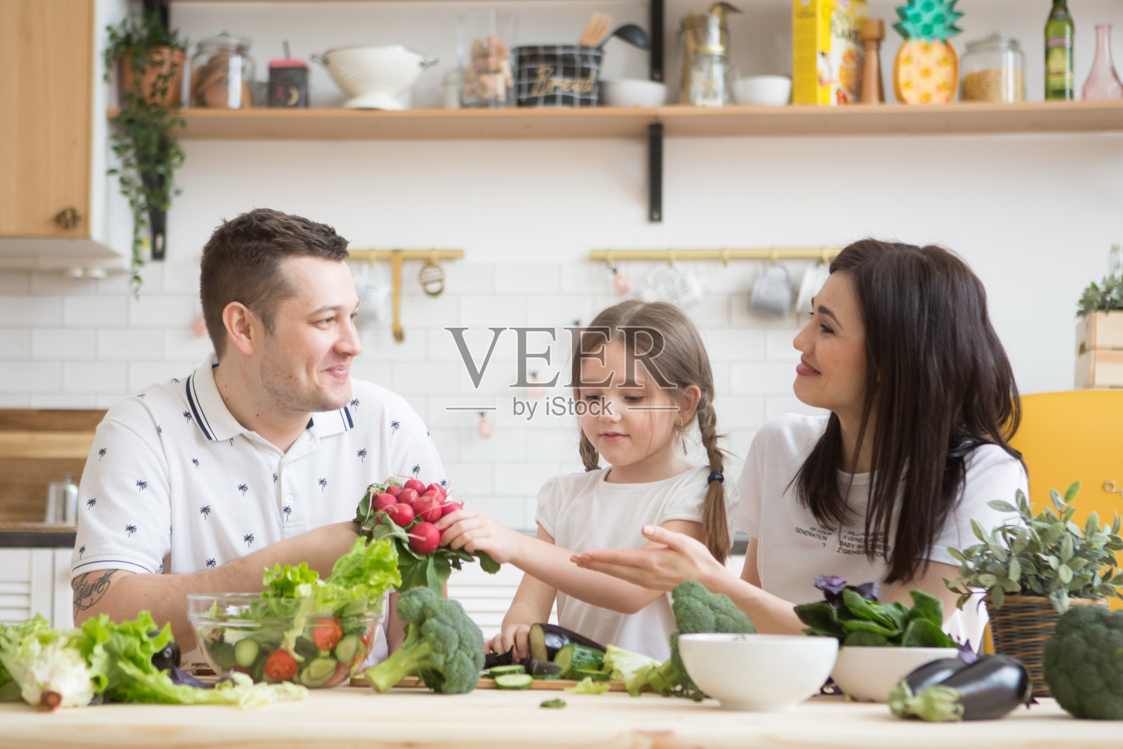 幸福的家庭的母亲。父亲和女儿在厨房里一起准备健康的蔬菜。帮助孩子成为父母。照片摄影图片