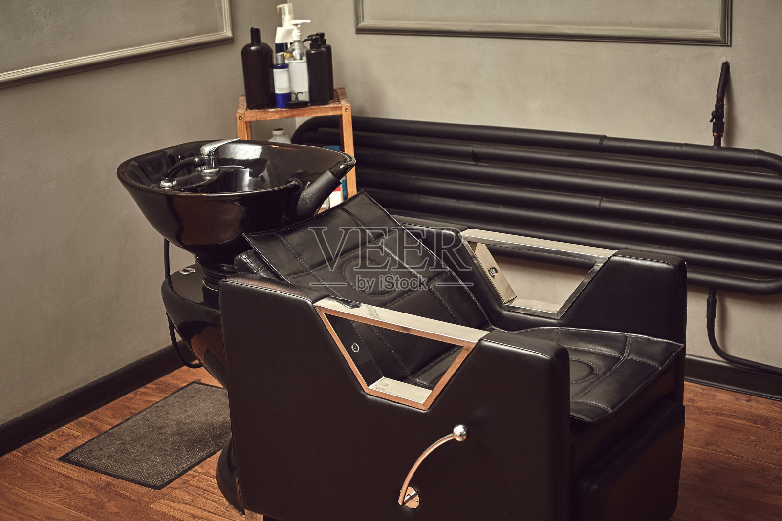 黑色皮革座椅与洗脸盆在理发店内部，毛巾和洗发水在一边。照片摄影图片