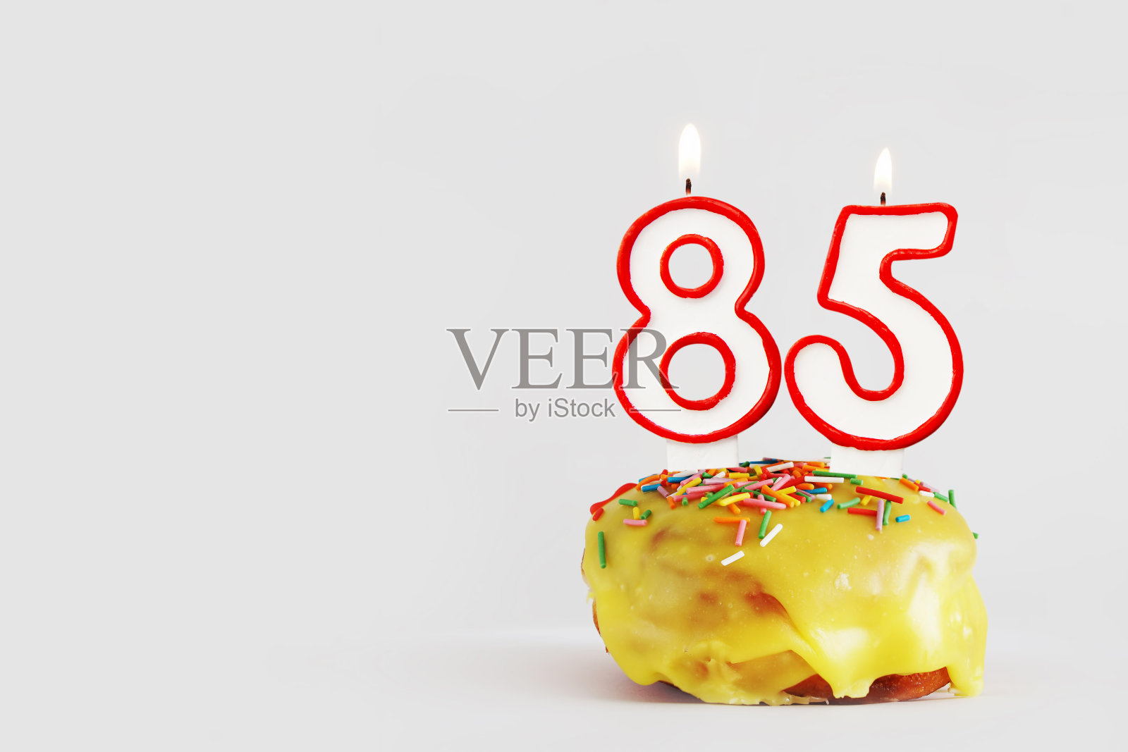 85周年纪念日。生日纸杯蛋糕与白色燃烧的蜡烛和红色边框形式的85数字。浅灰色背景与复制空间照片摄影图片