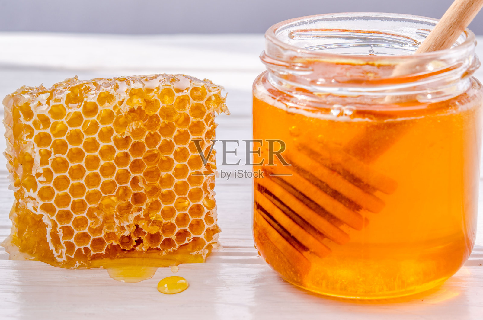 蜂蜜在一个玻璃罐里，里面有一个盛蜂蜜的木勺。有蜜滴的蜂巢照片摄影图片
