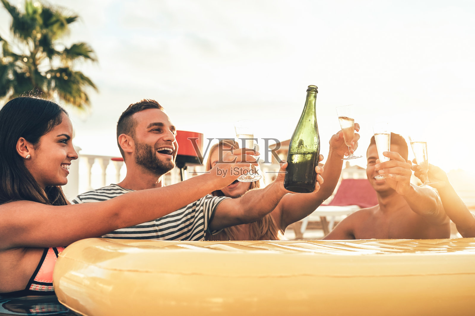 快乐的朋友在泳池派对上敬酒香槟-年轻人有乐趣喝起泡酒在豪华的热带海滩度假日落-假日，假期，夏季和青年的生活方式概念照片摄影图片