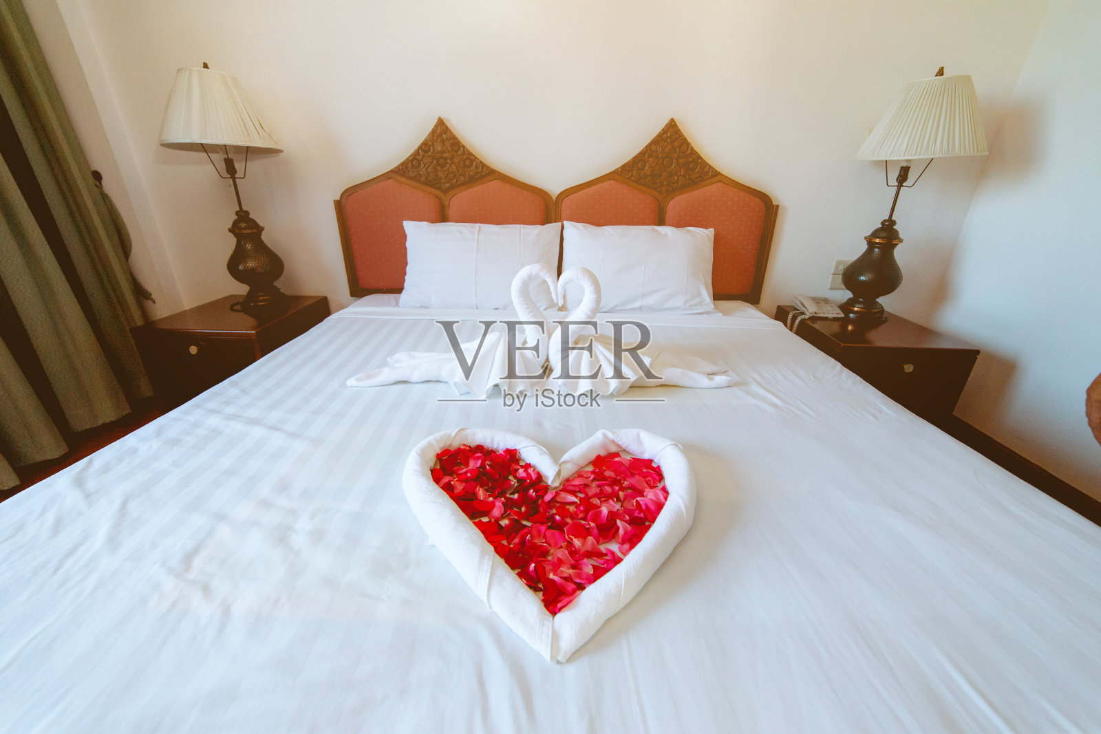 豪华酒店的床上装饰着玫瑰花瓣和双白天鹅形状的织物。照片摄影图片
