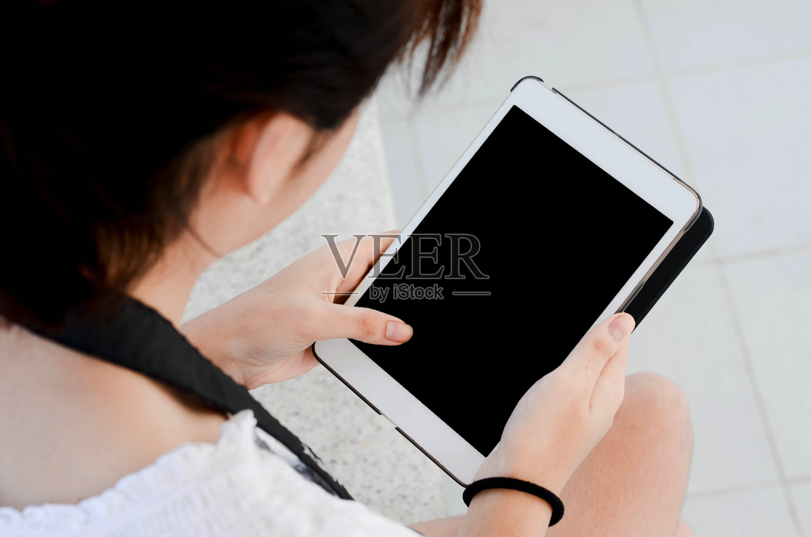 在公园里，一个女孩手持白色平板电脑，在社交网络上观看有趣的照片。照片摄影图片