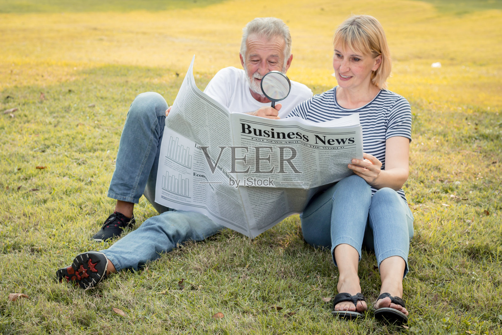 一对老夫妇正坐在草坪上看报纸。照片摄影图片