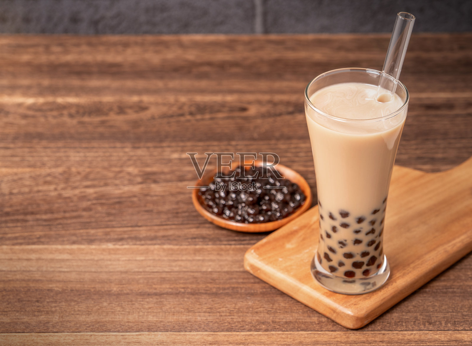 台湾流行饮品-珍珠奶茶配珍珠球在饮用玻璃和稻草，木桌子灰砖背景，近距离，拷贝空间照片摄影图片