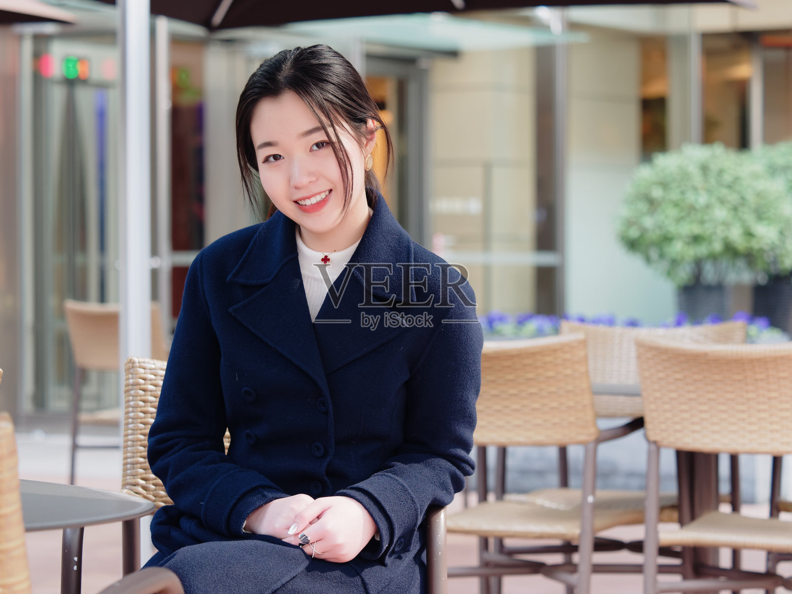 年轻的亚洲女人的肖像与黑色的长发坐在户外咖啡吧，微笑和快乐的现代城市背景。照片摄影图片