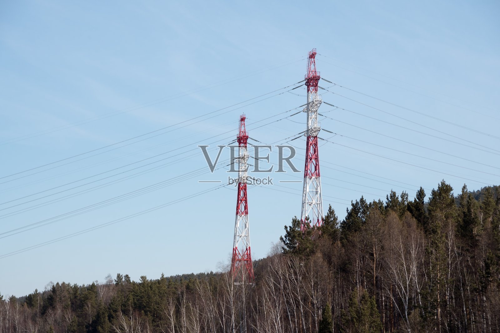 金属支撑的架空电力线为电力，在森林山丘上，背景是蓝天。照片摄影图片