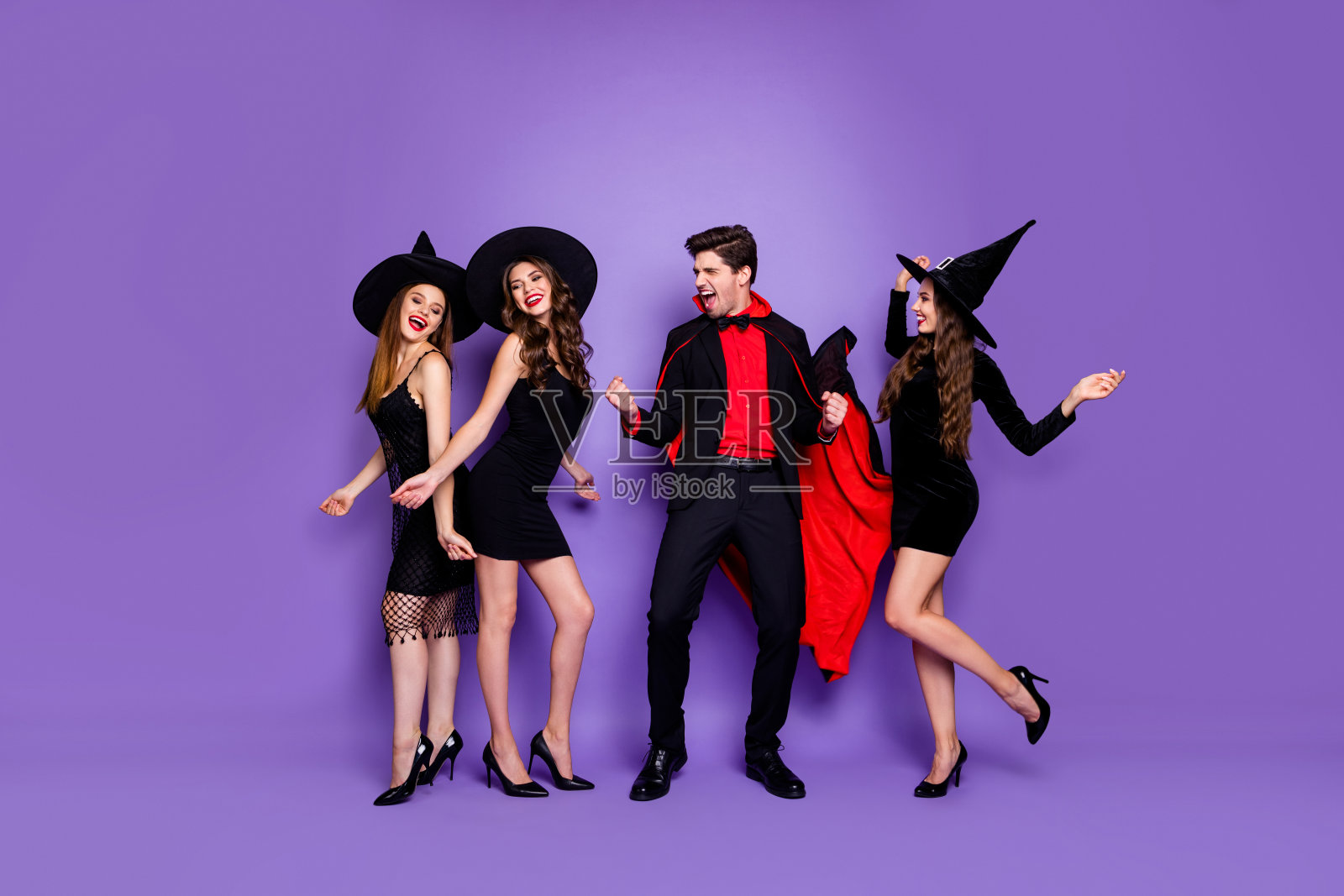 全尺寸照片的三个女巫女士和男巫在万圣节活动疯狂的跳舞穿着黑色礼服帽子和吸血鬼外套孤立的紫色背景照片摄影图片