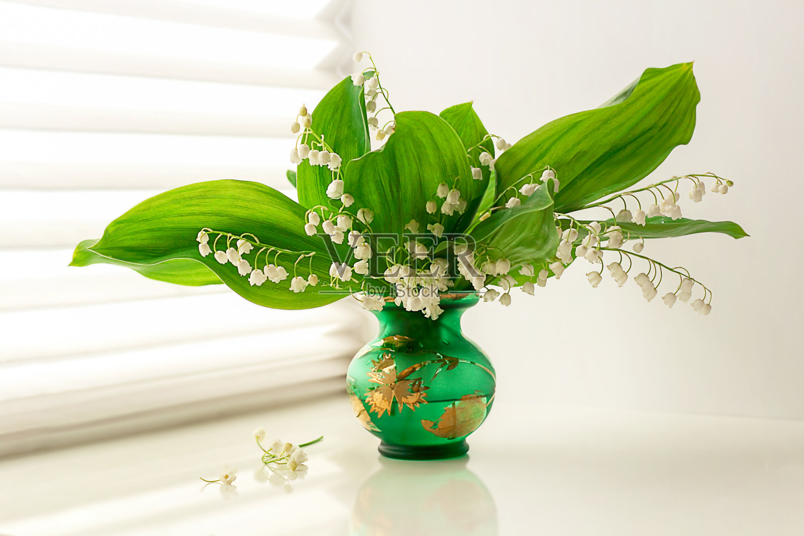 花瓶里装着铃兰花，背景是一扇带百叶窗的窗户，春花。有选择性的重点。照片摄影图片