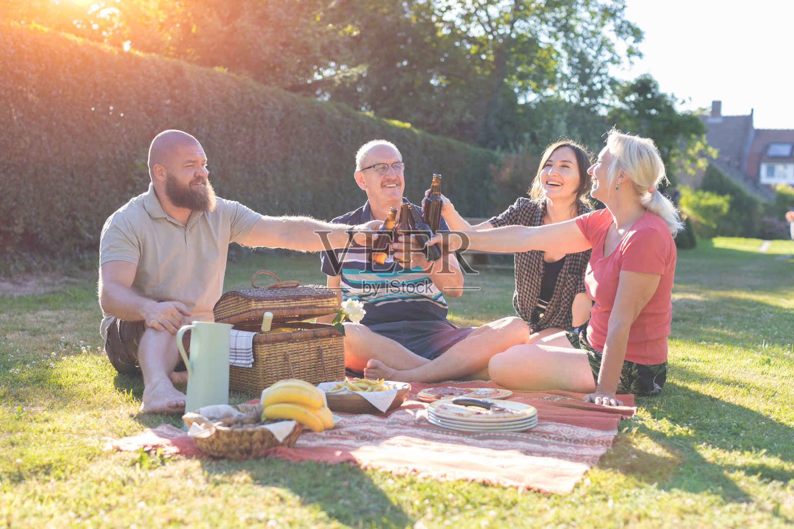 快乐的一家人在花园里野餐-不同年代的人们在一起用餐-孩子和父母玩得很开心，在夕阳下用啤酒瓶敬酒照片摄影图片
