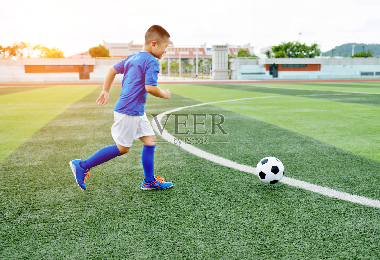 小男孩在操场上踢足球照片摄影图片